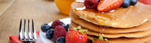 White plate full of pancakes with strawberries raspberries blueberries and honey